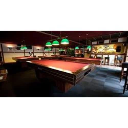 En svagt oplyst bar med poolborde i rød filt, grønne hængelamper over, stole og en bardisk i baggrunden.